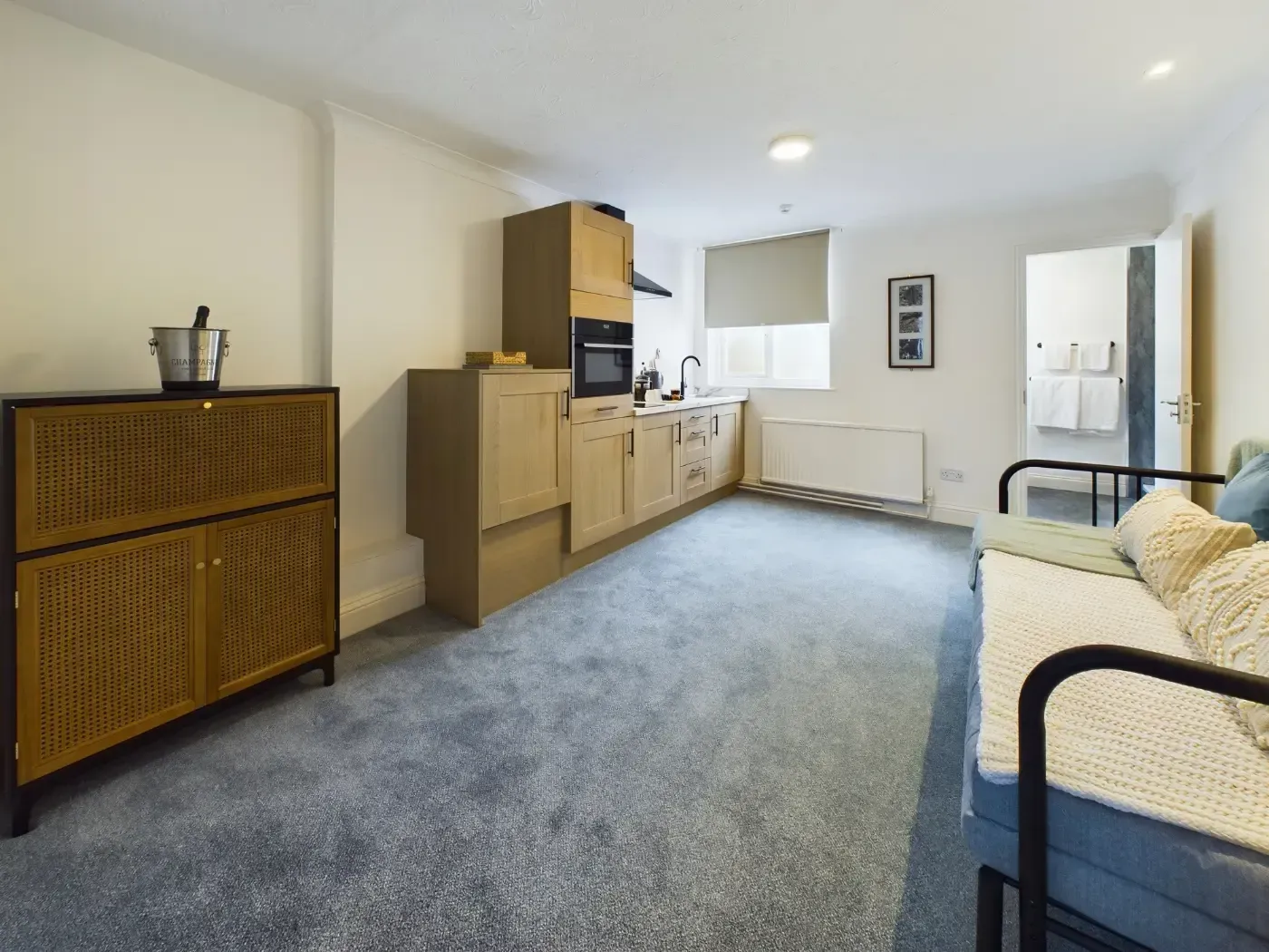 Bright living room with blue sofa, wooden storage unit, and kitchenette along the wall