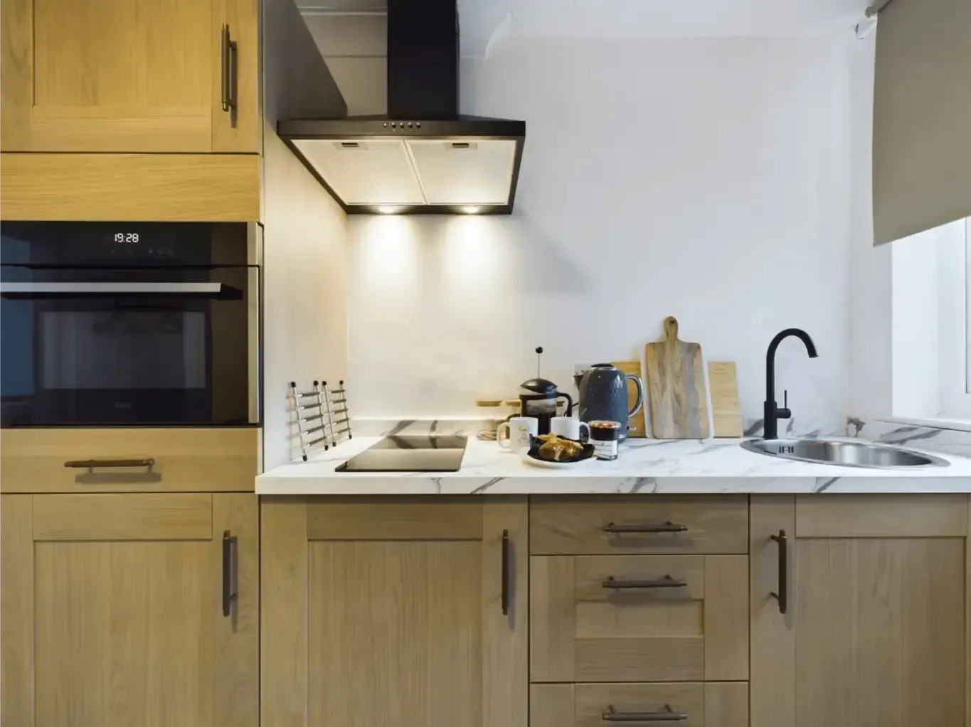 Modern kitchen with wood cabinets, marble countertop, stove, sink, and black range hood