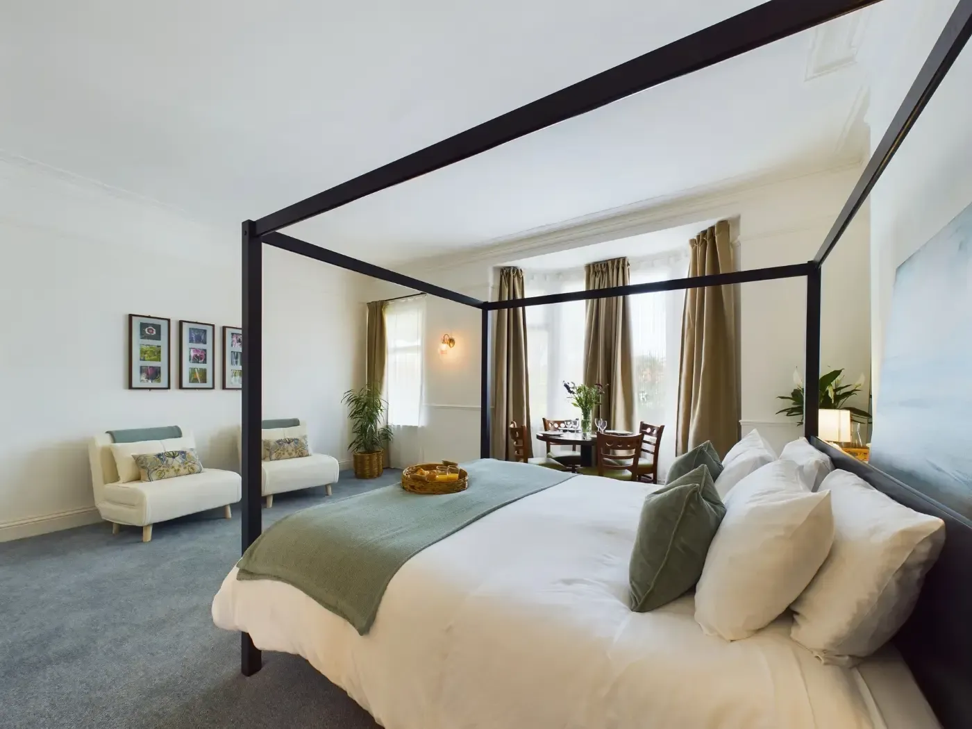 Bright modern bedroom with canopy bed, green accents, armchair, and dining area by tall windows