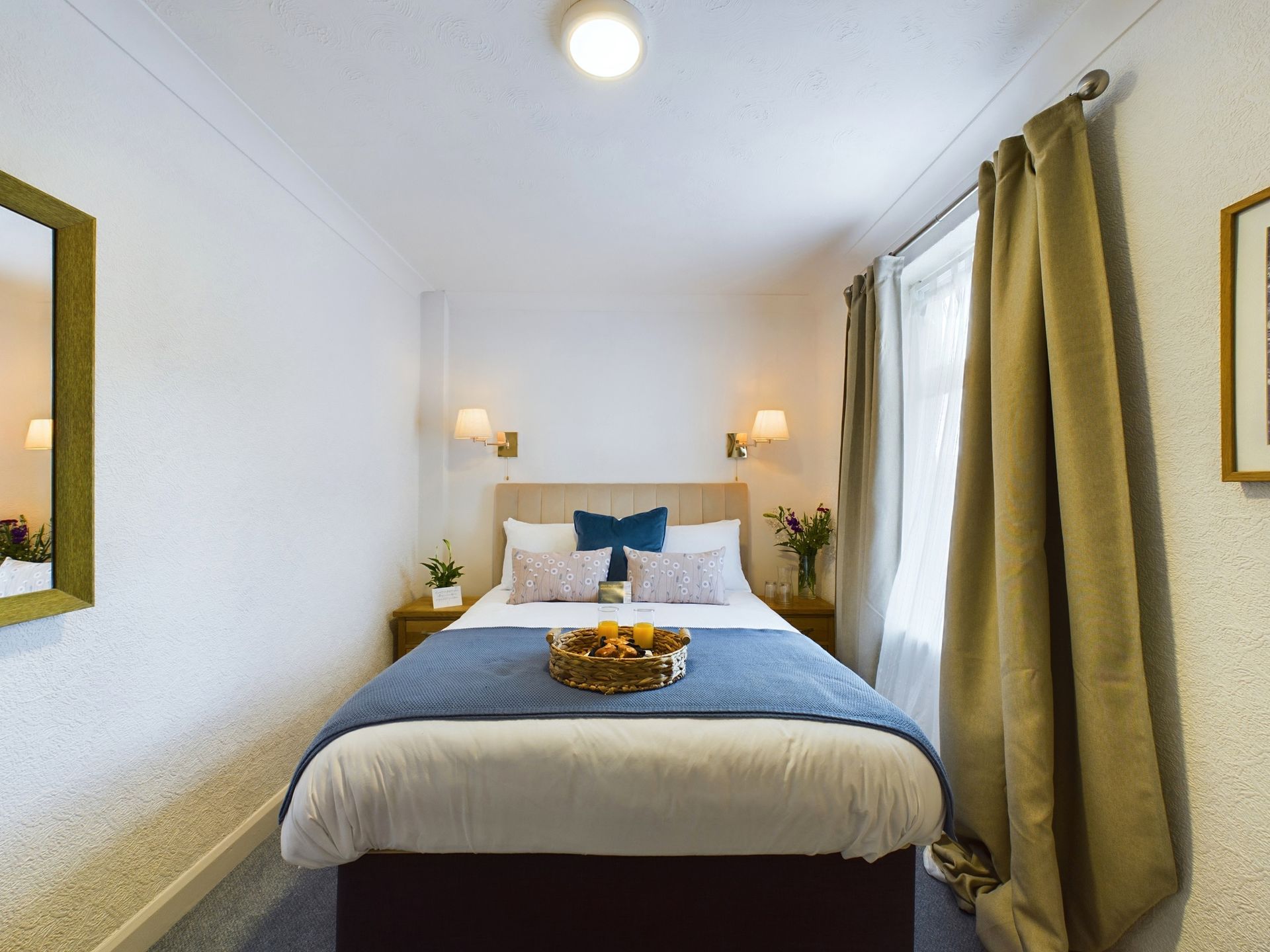Cozy bedroom with a neatly made bed, white walls, blue bedding, bedside lamps, and green curtains