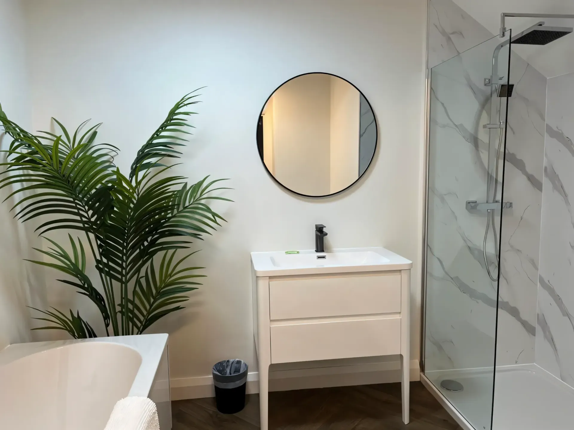 Modern bathroom with white vanity, round mirror, glass shower, and a potted plant