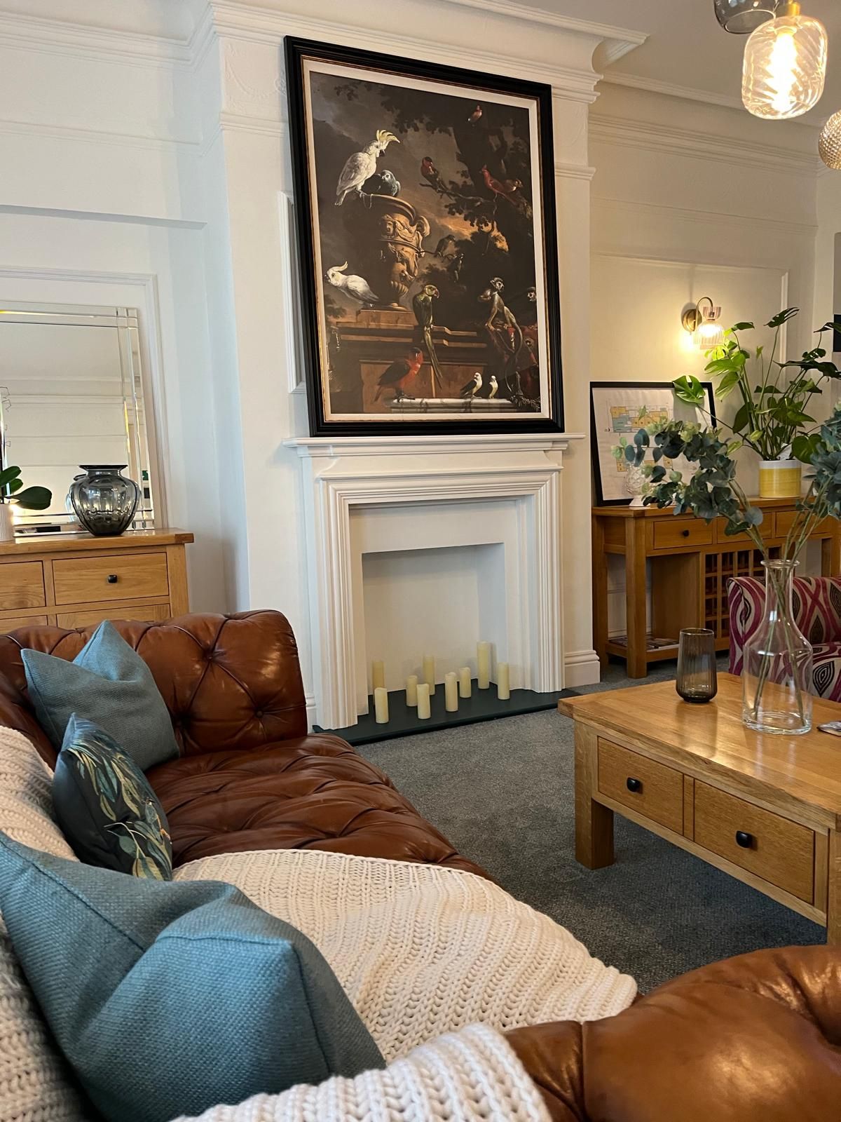 Cozy living room with brown leather sofa, teal pillows, white fireplace, and framed art above the mantel