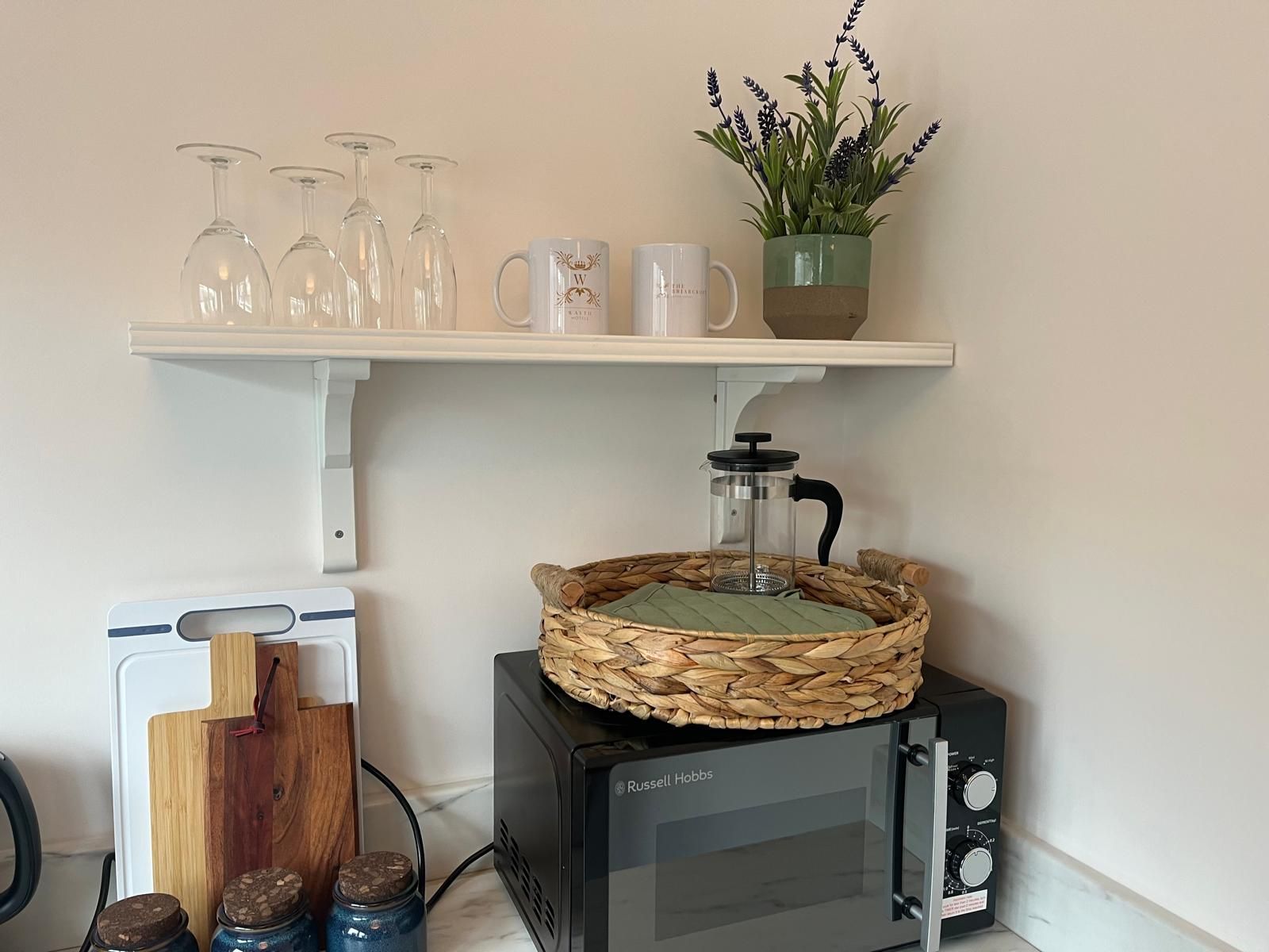 Kitchen shelf with glassware, mugs, a potted plant, and a black toaster oven with a basket on top