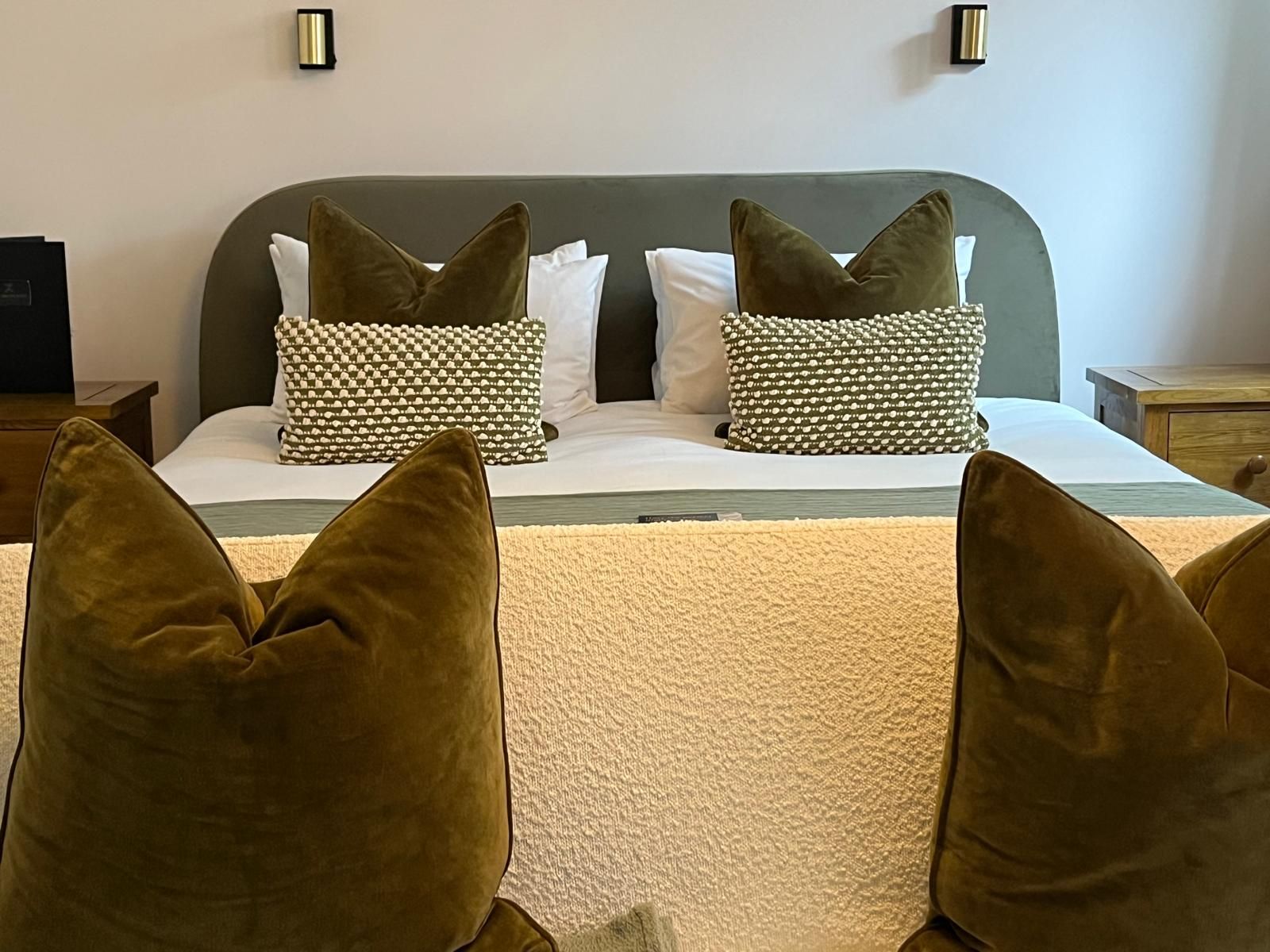 Cozy bed with olive pillows, white bedding, and a beige throw in a softly lit bedroom