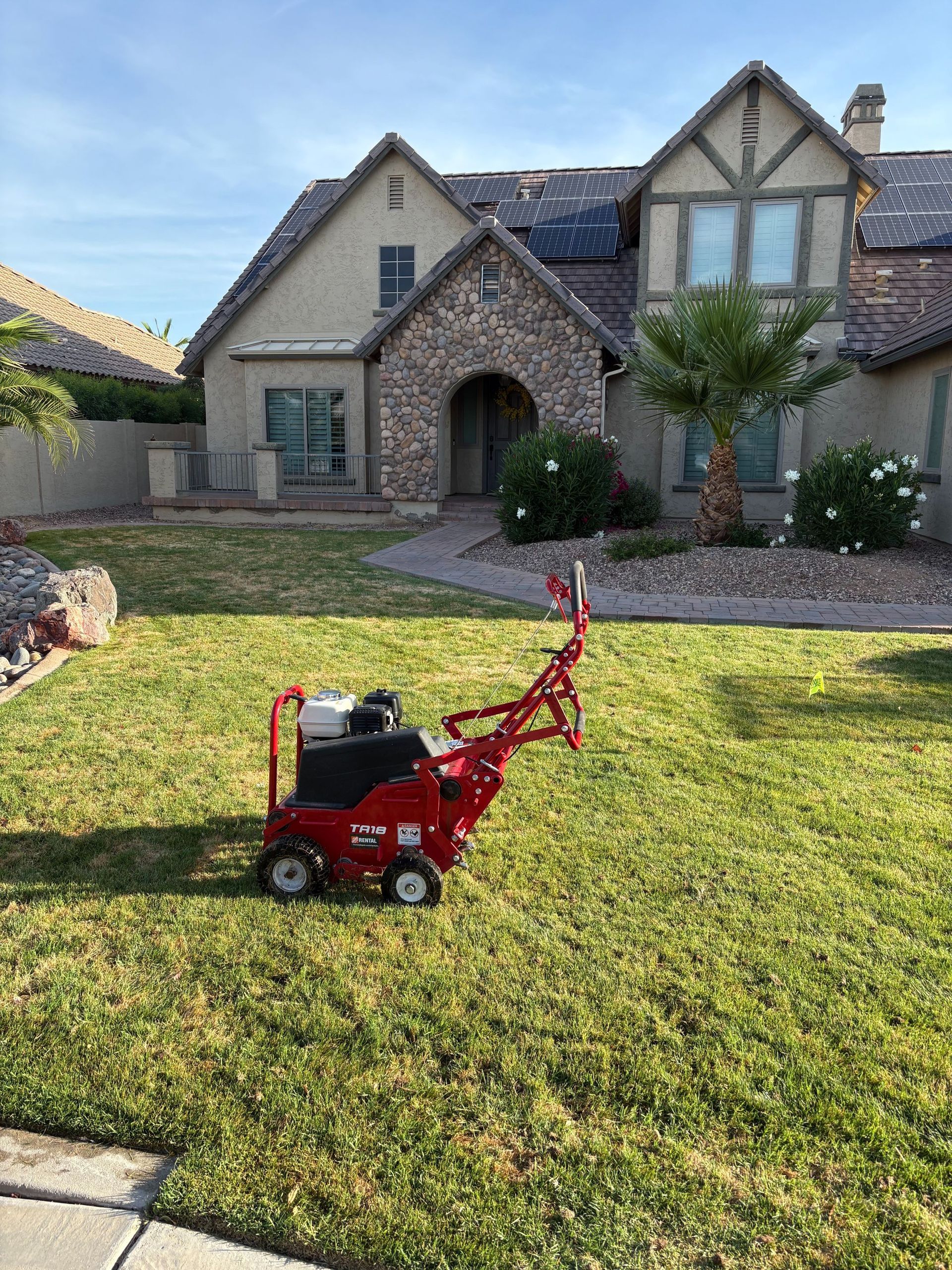Red lawn aerator on green grass in front of a house.