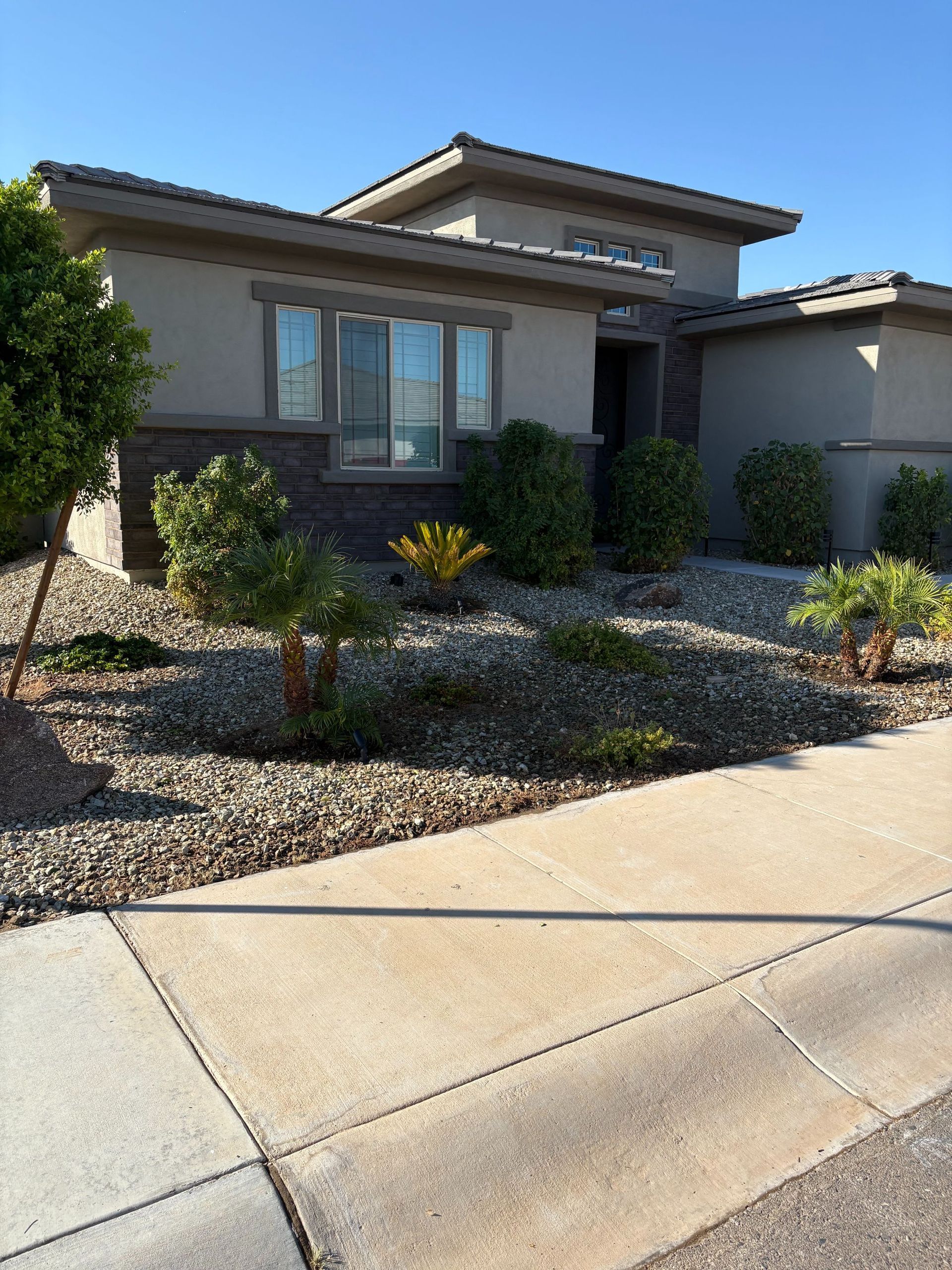 A beige house with a landscaped front yard, rock and shrubbery, and a sidewalk.