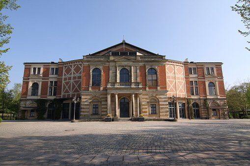 Brick and sandstone theater building with columns and a central balcony, under a clear blue sky.