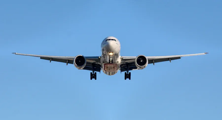 Airplane landing, coming toward the viewer, against a clear blue sky.