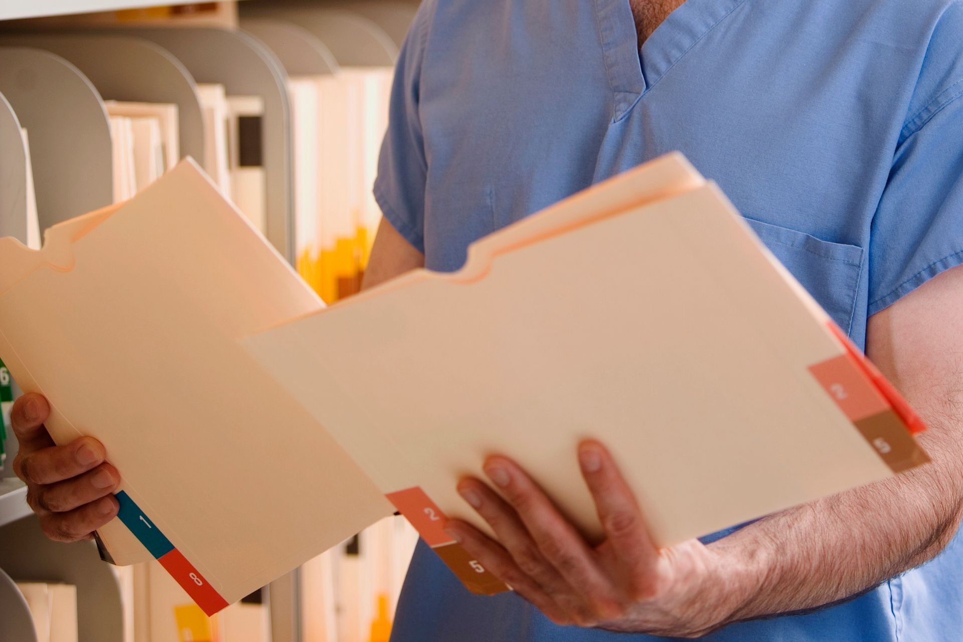 A man in a blue scrub is holding a folder in his hands.