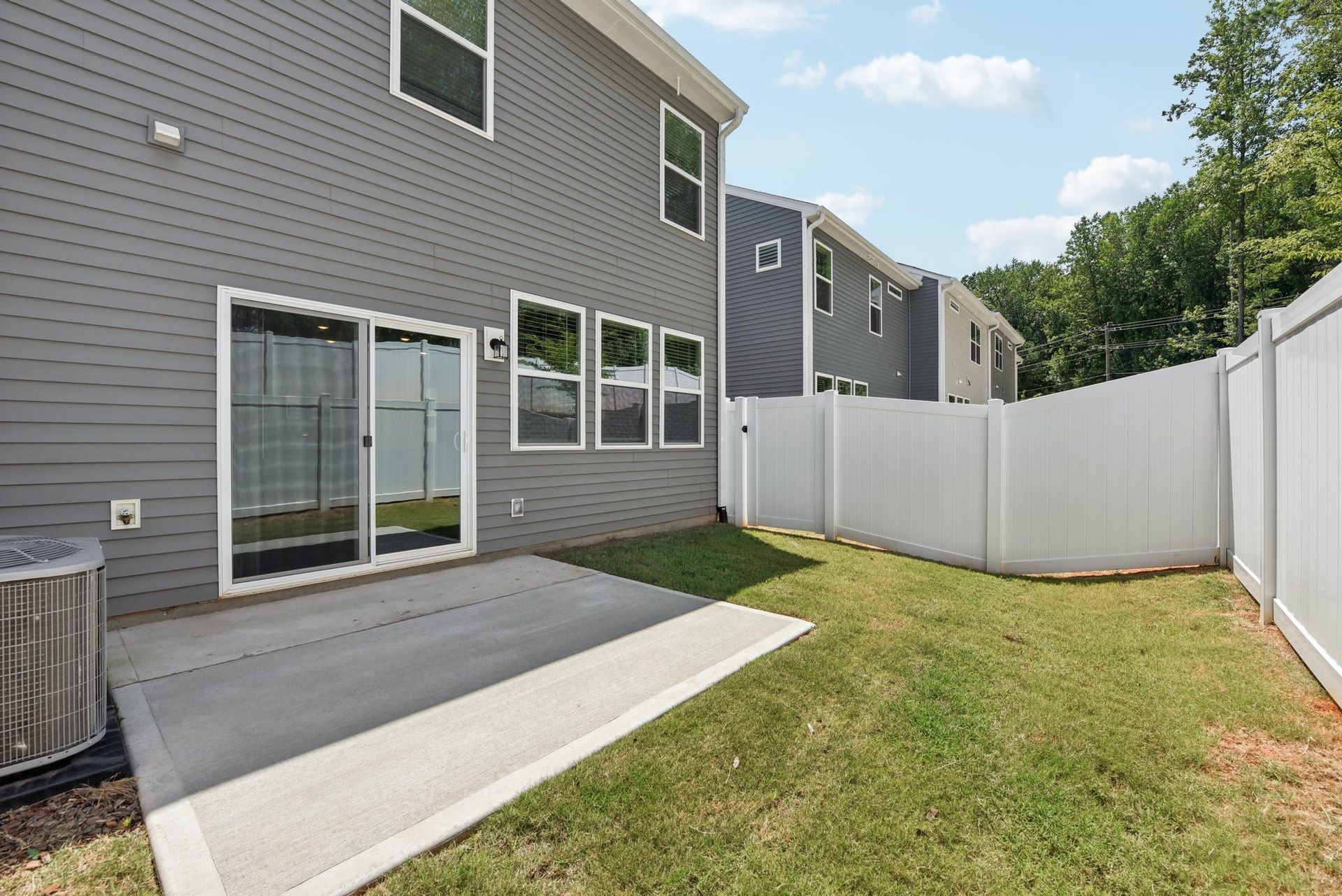 Backyard patio with sliding door, gray siding, and white privacy fence.