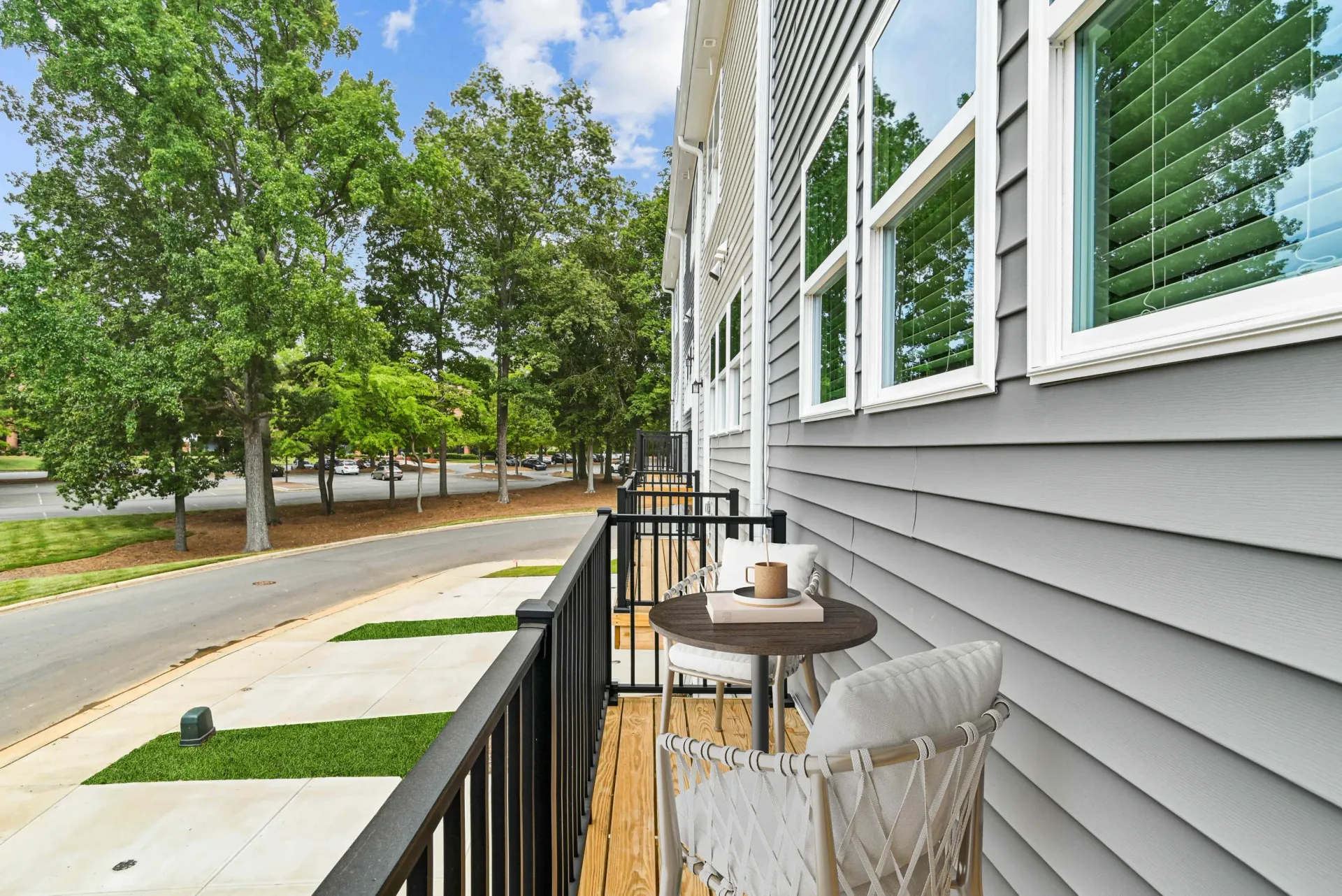 Balcony of a gray apartment building with seating overlooking a tree-lined street.