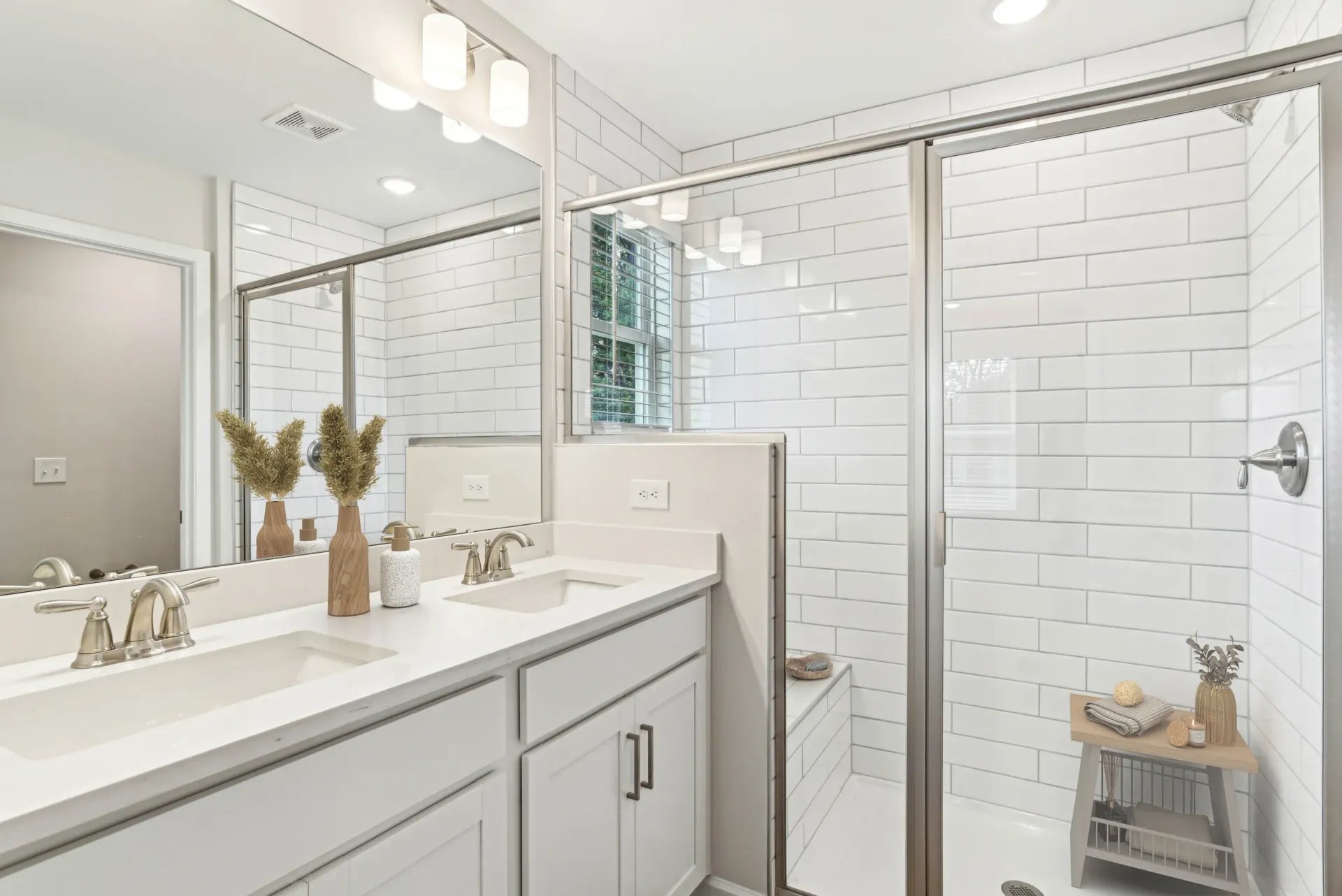 Bright white bathroom with a double vanity, large mirror, and glass-enclosed shower.