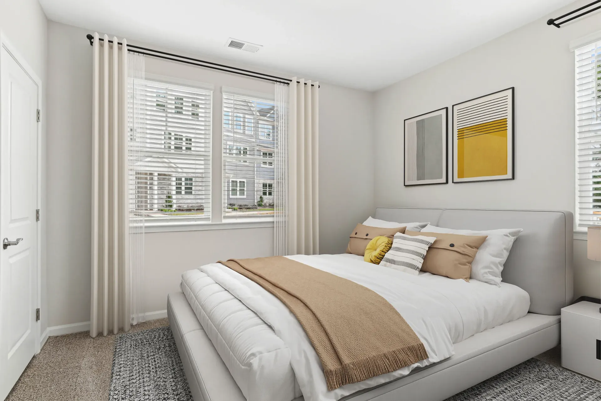 Bright bedroom with a gray upholstered bed, white bedding, beige throw, and large windows with sheer curtains.