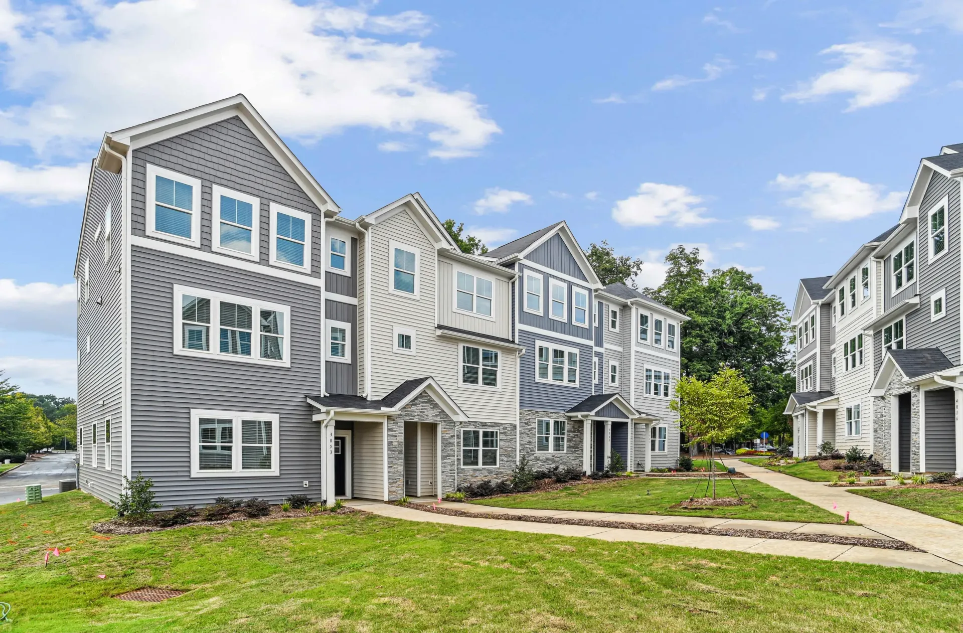 Row of modern townhome buildings with gray-blue siding, white trim, and landscaped lawns.