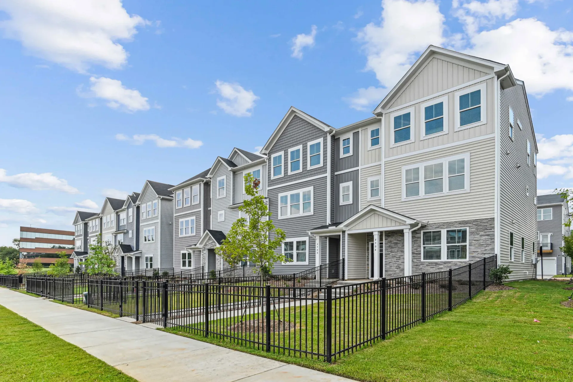 Exterior view of modern townhouse-style apartment buildings with a lawn and walkway.