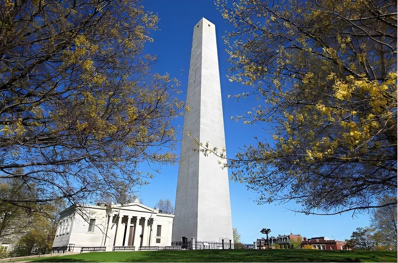 The Bunker Hill Monument in Charlestown, Massachusetts, a tall granite obelisk standing near a classic museum building.
