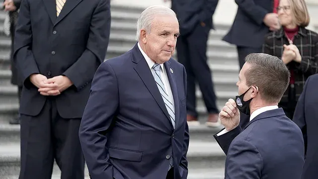 A man in a suit and tie is talking to another man in a mask.