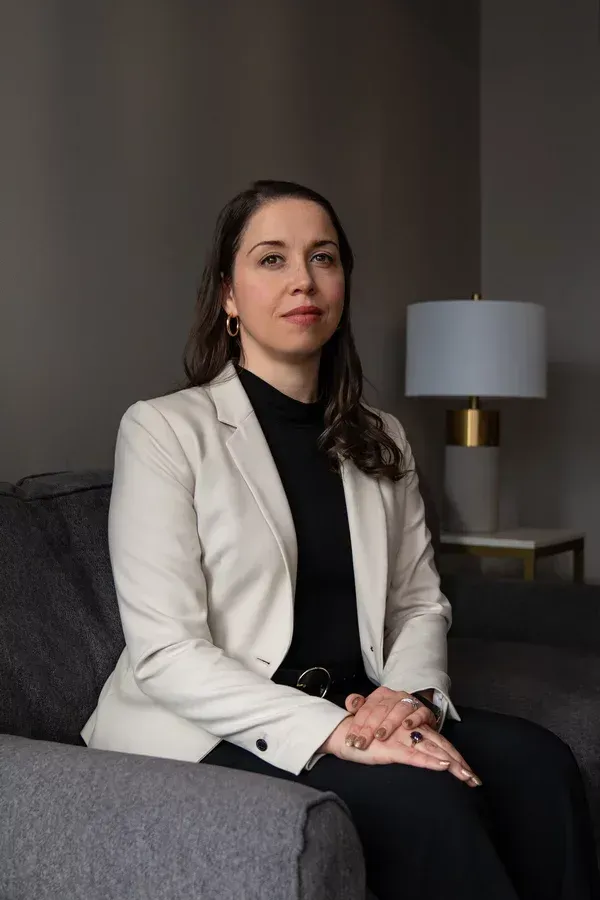 A woman is sitting on a couch with her hands folded.