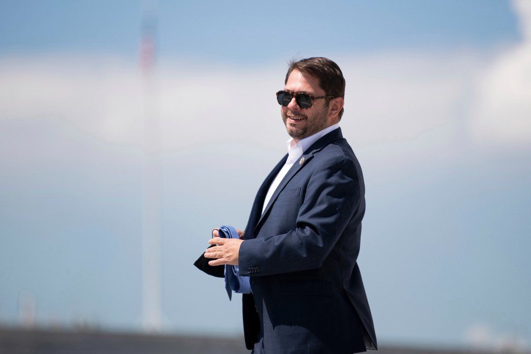A man in a suit and sunglasses is standing in front of a wind turbine.