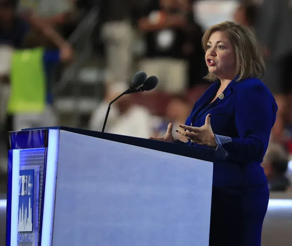 A woman in a blue suit is giving a speech at a podium