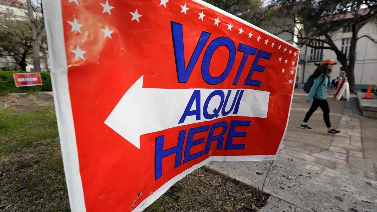 A woman is walking past a vote aqui here sign.