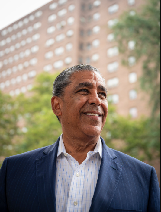 A man in a suit is smiling in front of a building.
