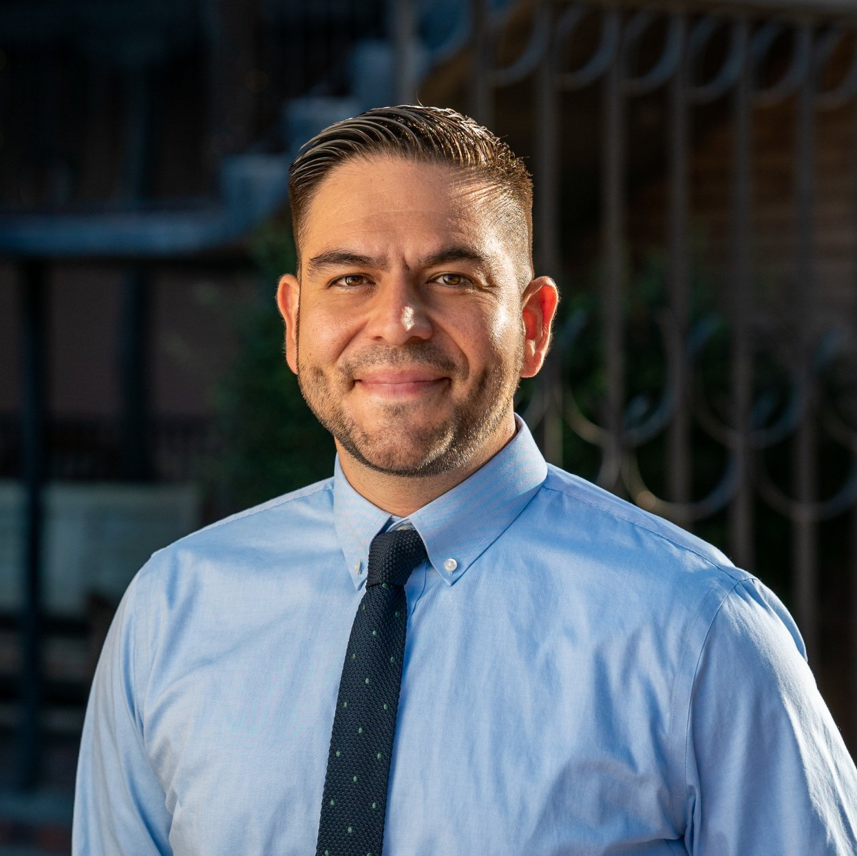 A man in a blue shirt and tie is smiling for the camera.