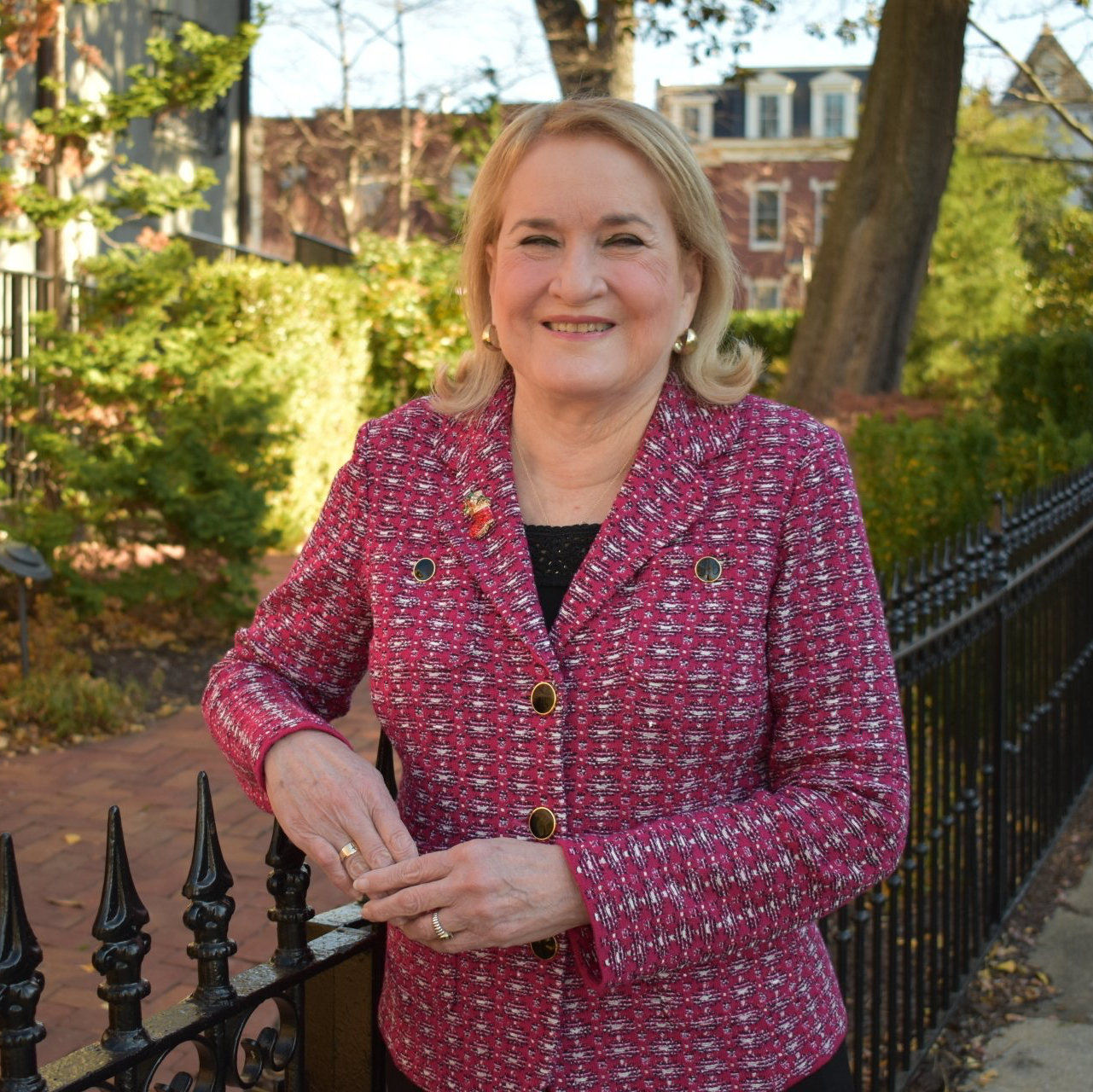 A woman in a pink jacket is standing next to a fence.