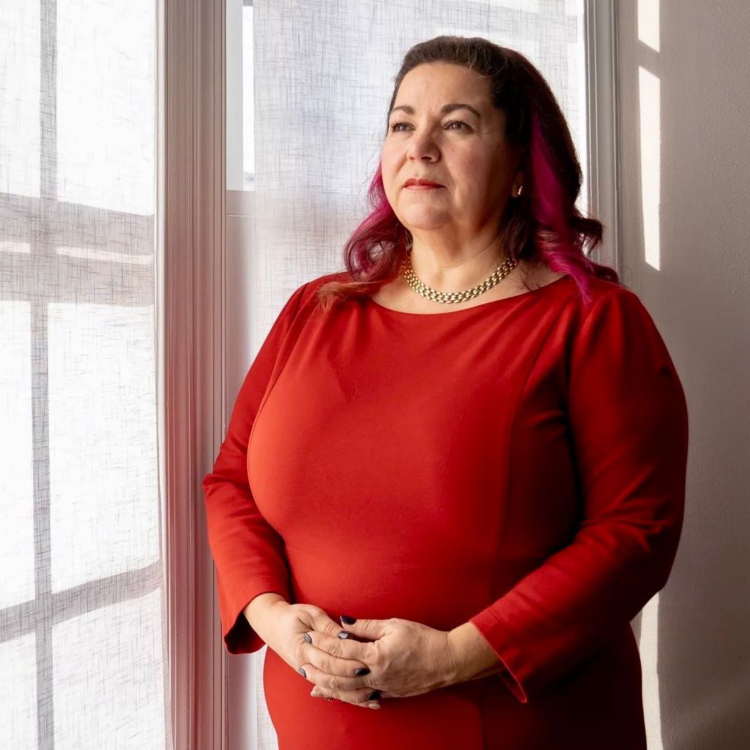 A woman in a red dress is standing in front of a window.