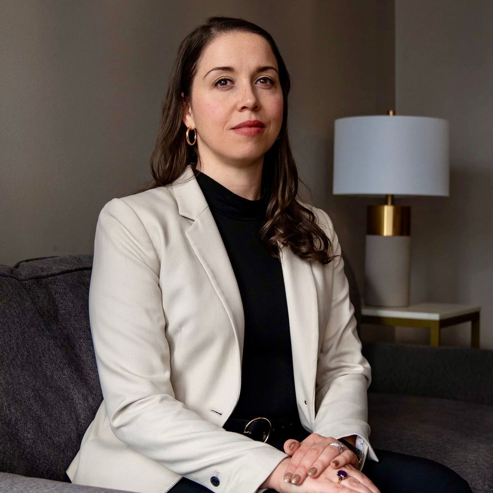 A woman in a white jacket and black shirt is sitting on a couch.