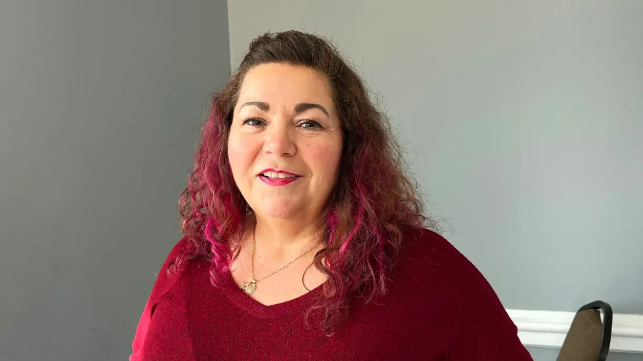 The woman is wearing a red sweater and has pink hair.