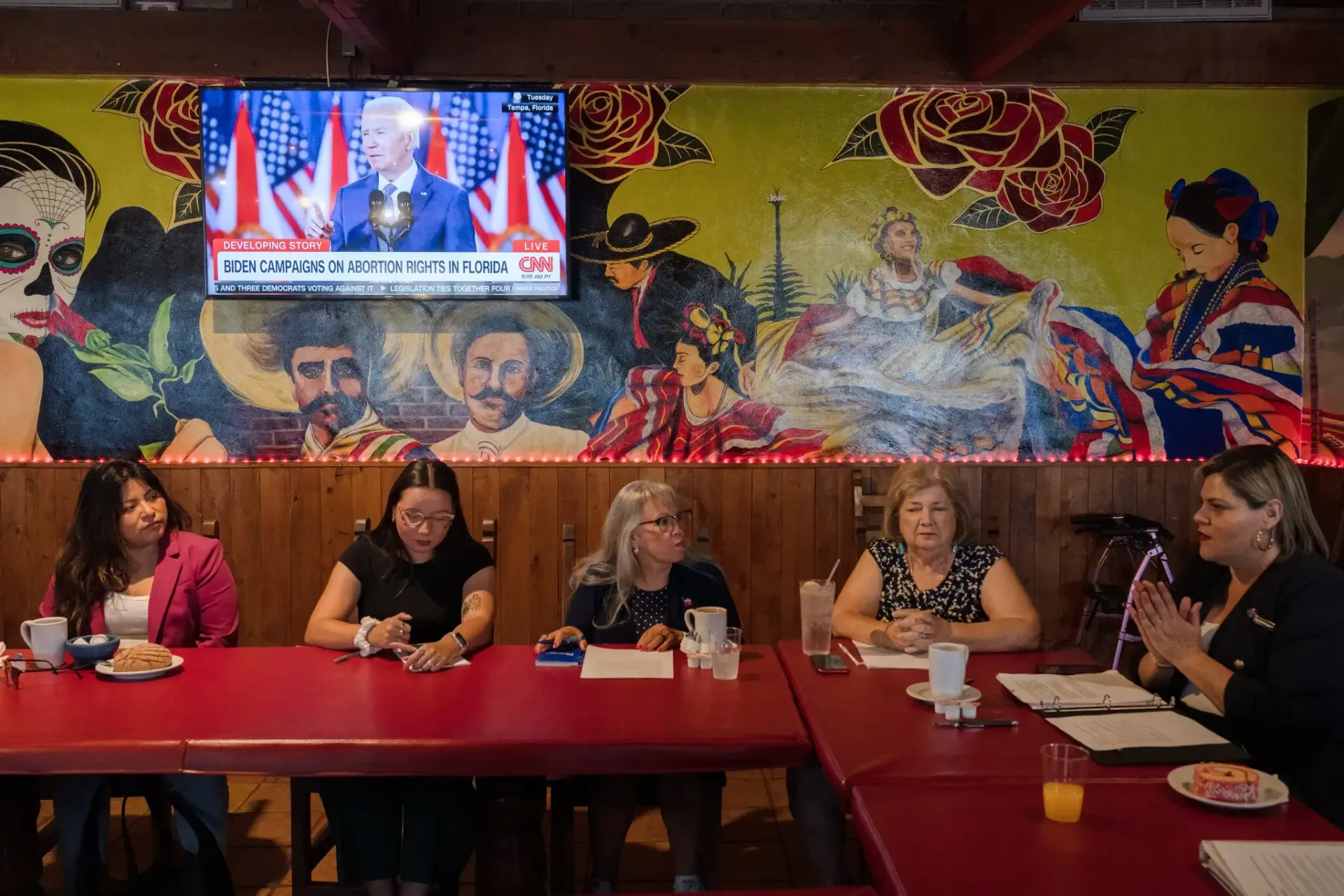 A group of women are sitting at a table in front of a mural.