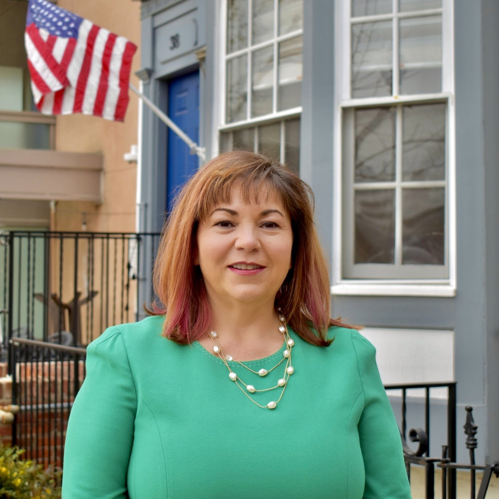 A woman in a green dress stands in front of an american flag