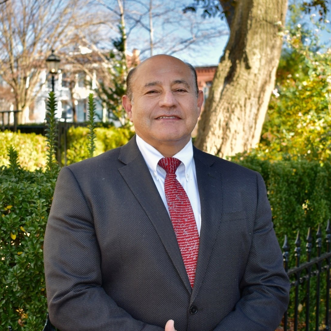 A man in a suit and tie is standing in front of a tree