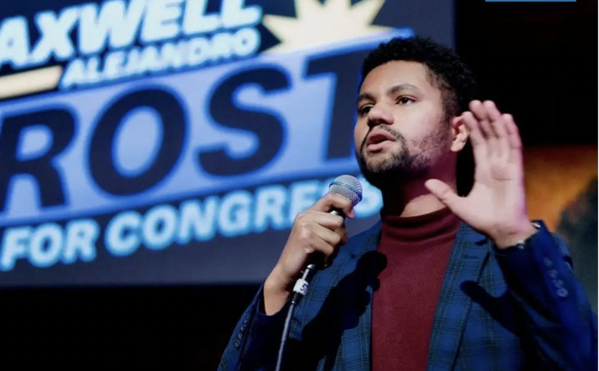 A man speaking into a microphone in front of a sign that says axwell rost for congress