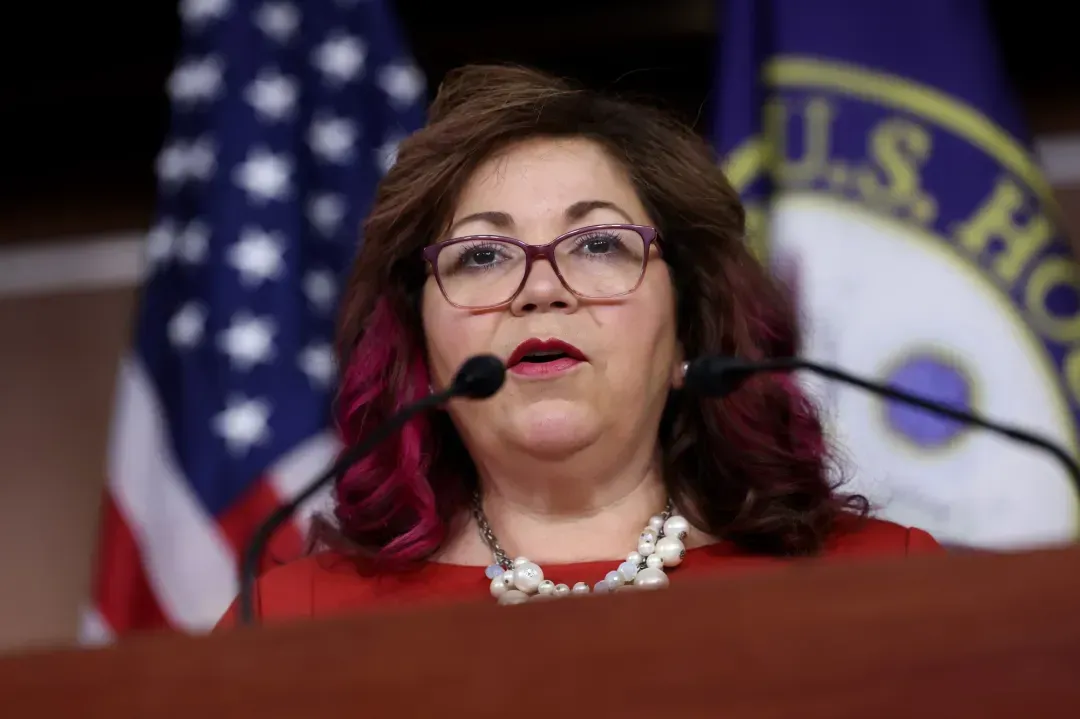 A woman is speaking into a microphone in front of an american flag.