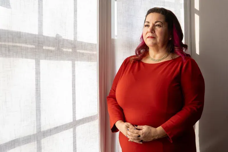 A woman in a red dress is standing in front of a window.