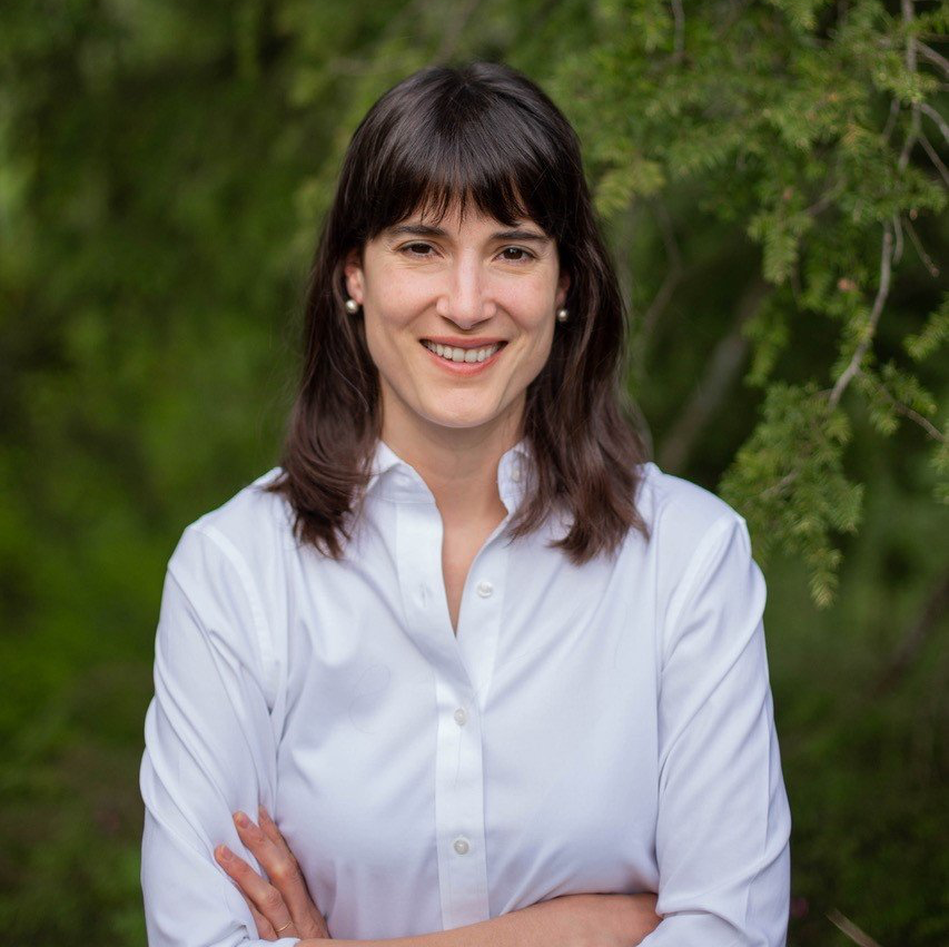 A woman in a white shirt is smiling with her arms crossed.