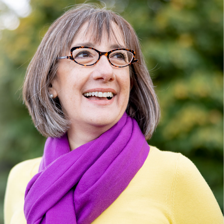A woman wearing glasses and a purple scarf is smiling.