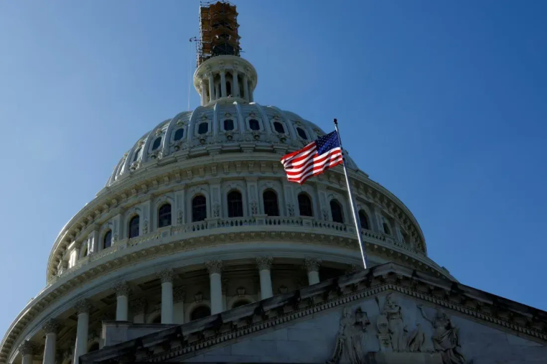 Looking up at the dome of the capitol building with an american flag flying in front of it.
