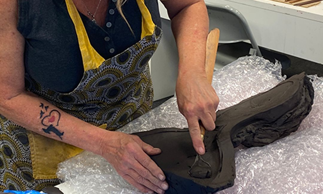 A woman with a tattoo on her arm is working on a piece of clay.
