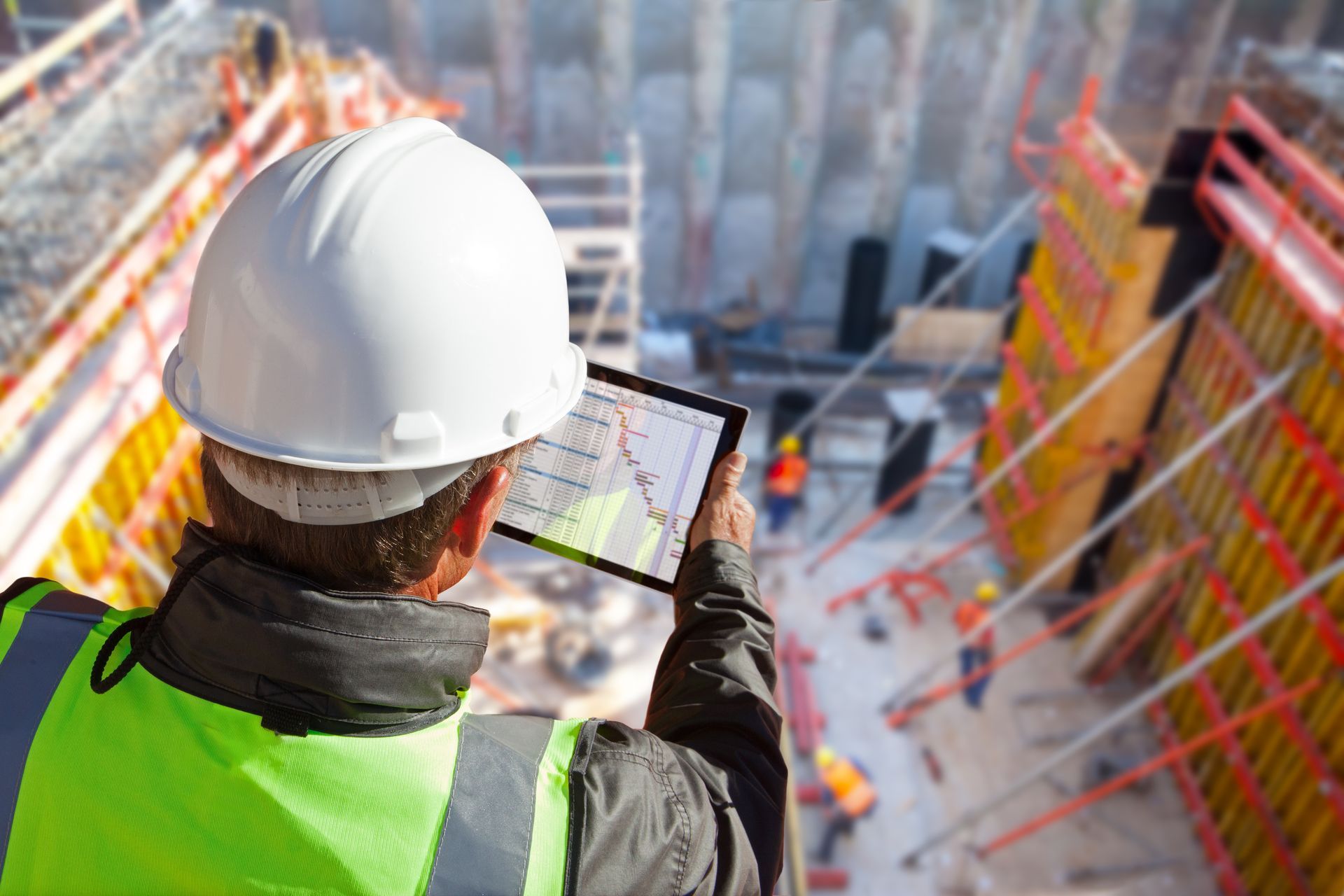 A construction worker in a hard hat holds a tablet, reviewing plans on a construction site. A construction worker in a hard hat holds a tablet, reviewing plans on a construction site.