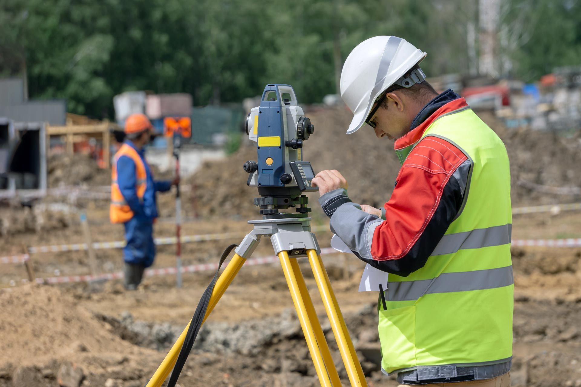 A surveyor using a total station on a tripod at a construction site while recording measurements A surveyor using a total station on a tripod at a construction site while recording measurements