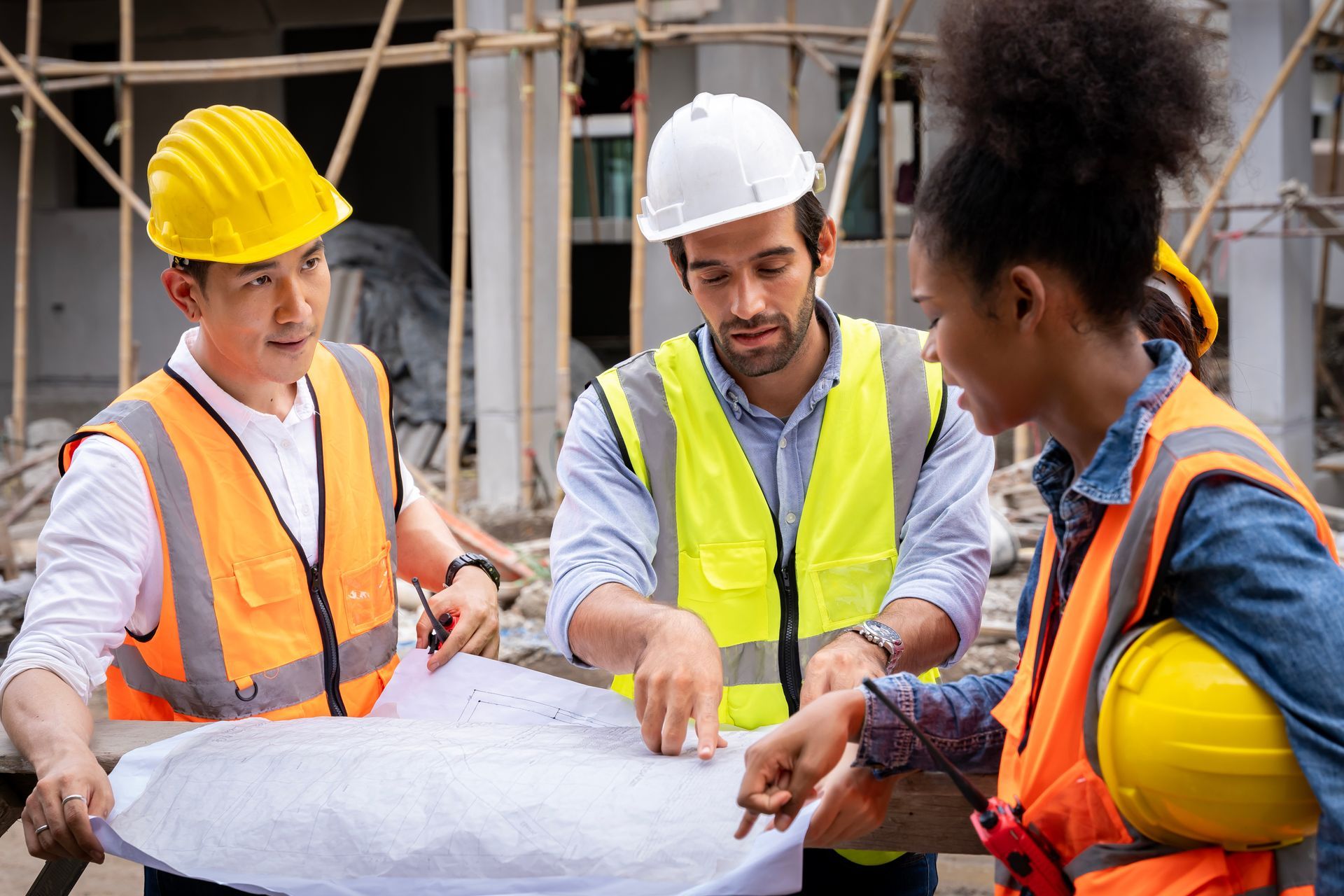 A team of civil engineers is checking and discussing a blueprint at a construction site.