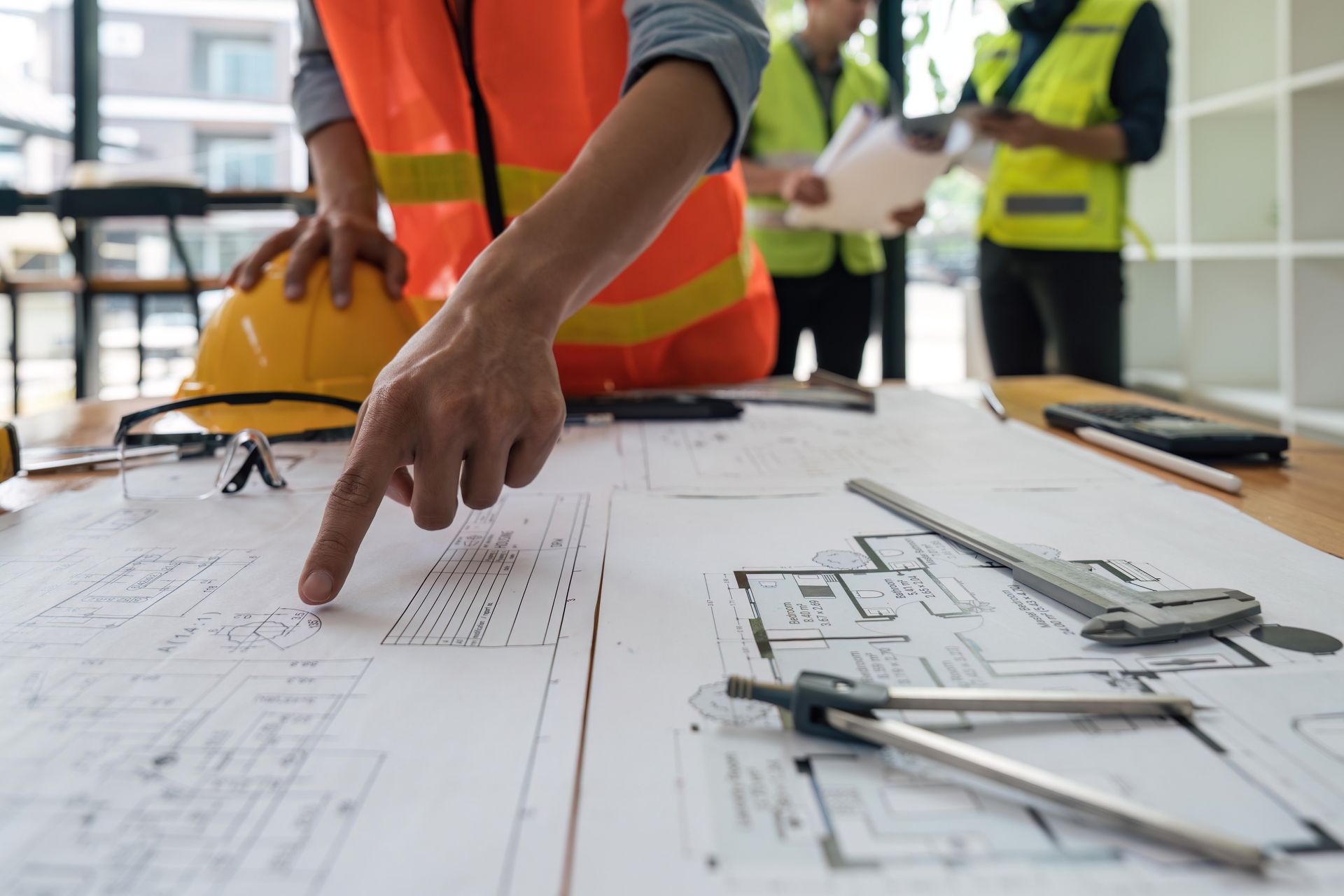 An engineer points at a blueprint spread out on a table with instruments. An engineer points at a blueprint spread out on a table with instruments.