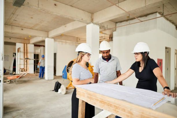 Three people in hard hats reviewing blueprints at a construction site.