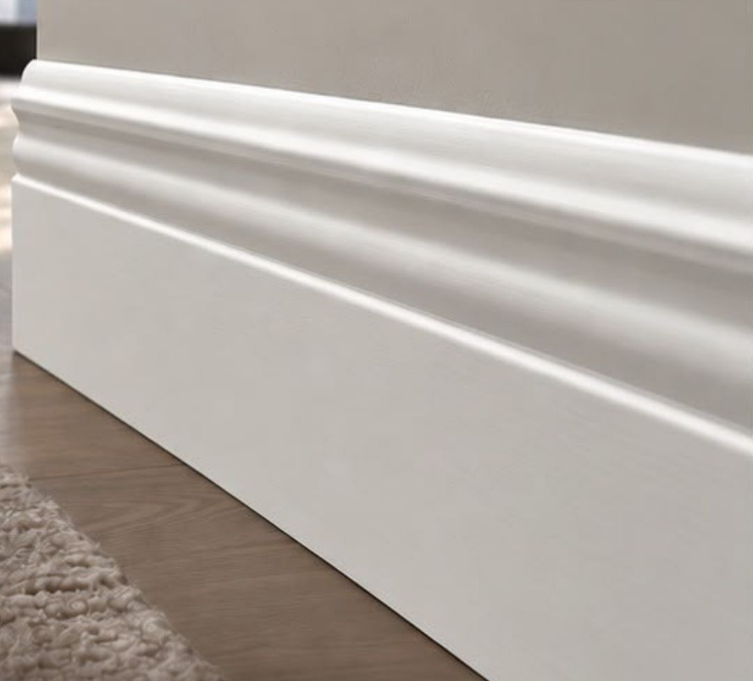White baseboard trim, 5.25 inches tall, against a wood grain floor and brown wall. WM 5180