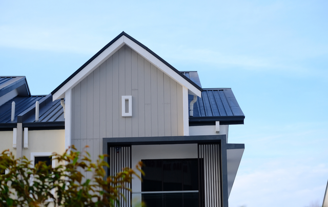 A modern house exterior featuring a gray gable, dark metal roof, and a minimalist balcony under a clear blue sky.