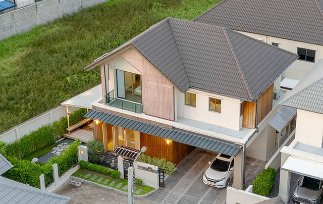 An aerial view of a two-story modern house with a dark tiled roof, wooden accents, a carport, and a small garden.