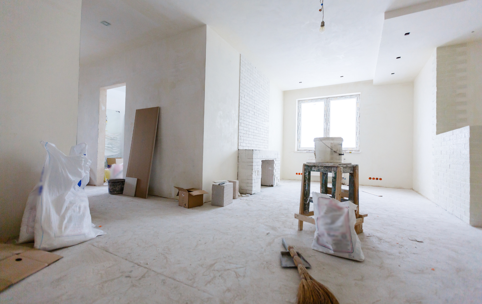 An empty room under construction with white walls, a bare floor, construction supplies, and tools.